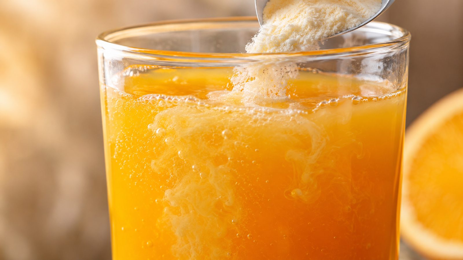 Close-up de colágeno em pó branco se dissolvendo em um copo de suco de laranja